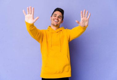 Mor arka planda izole edilmiş genç beyaz adam on numarayı elleriyle gösteriyor..