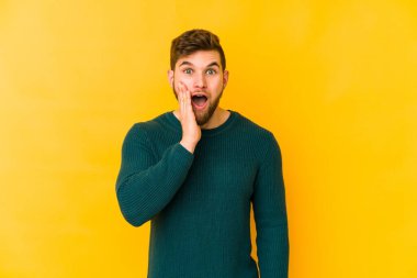 Sarı arka planda izole edilmiş genç beyaz adam yüksek sesle bağırıyor, gözleri açık ve elleri gergin tutuyor..