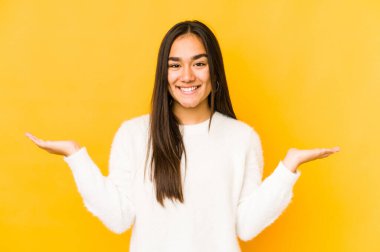 Sarı arka planda izole edilmiş genç bir kadın kollarıyla ölçek oluşturuyor, mutlu ve kendinden emin hissediyor..