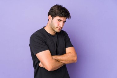 Mor arka planda izole edilmiş, hoşnutsuzca kaşlarını çatmış, kollarını kavuşturmuş genç bir adam..