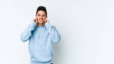 Beyaz arka planda izole edilmiş genç beyaz bir adam parmaklarıyla kulaklarını kapatıyor, gürültülü bir ortam yüzünden stresli ve çaresiz..