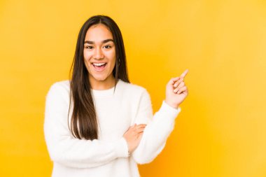 Sarı arka planda izole edilmiş genç bir kadın işaret parmağıyla işaret ederek gülümsüyor..