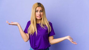 Mor arka planda izole edilmiş genç sarışın kadın. Kafası karışmış ve omuz silkiyor. Kopya alanını tutmak için..