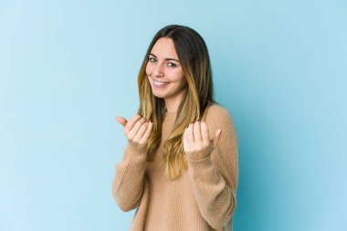Mavi arka planda izole edilmiş genç beyaz kadın sanki seni davet ediyormuş gibi seni işaret ediyor..
