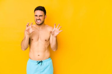 Sarı arka planda mayosu olan genç, beyaz bir adam. Tırnaklarını hareket ettiren genç, beyaz bir adam. Saldırgan bir hareket..