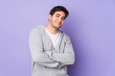 Mor arka planda izole genç bir adam kendinden emin, kararlılıkla kollarını kavuşturuyor..