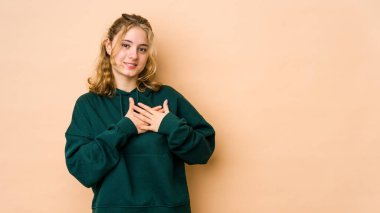 Bej arka planda izole edilmiş beyaz bir kadın. Dostane bir ifadeye sahip. Avuçlarını göğsüne bastırıyor. Aşk konsepti.