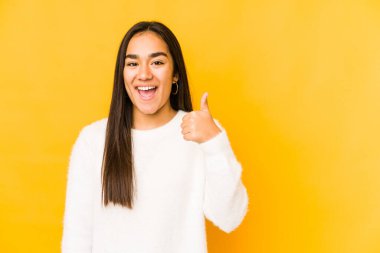 Sarı arka planda izole edilmiş genç bir kadın gülümsüyor ve baş parmağını kaldırıyor.