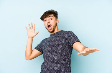 Genç Arap bir adam mavi bir arka planda izole edildi. Yakın bir tehlike nedeniyle şok oluyor.