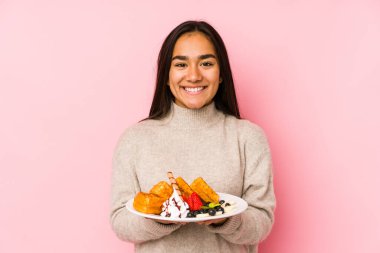 Elinde waffle tutan genç Asyalı kadın mutlu, güler yüzlü ve neşeli..