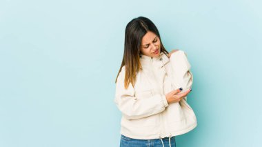 Genç bir kadın mavi arka planda izole edilmiş, dirsek masajı yapıyor, kötü bir hareketin ardından acı çekiyor..