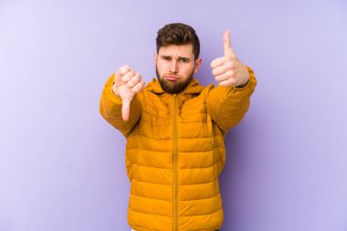 Mor arka planda izole edilmiş genç adam, baş parmağını kaldırıyor, zor bir seçim konsepti.