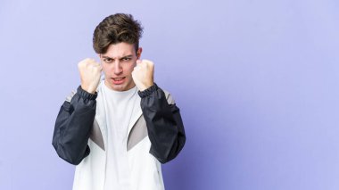 Mor arka planda izole edilmiş genç beyaz adam yumruğunu kameraya gösteriyor, agresif yüz ifadesi var..