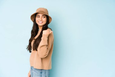 Mavi arka plan noktalarına izole edilmiş şapka takan genç Hintli kadın başparmak uzakta, gülüyor ve kaygısız..