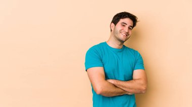 Bej arka planda izole genç bir adam kendinden emin, kararlılıkla kollarını kavuşturuyor..