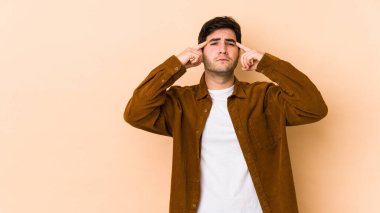 Bej arka planda izole edilmiş genç bir adam bir göreve odaklanmış, işaret parmaklarını başını işaret ediyor..