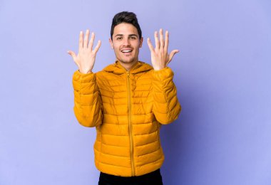 Mor arka planda izole edilmiş genç beyaz adam on numarayı elleriyle gösteriyor..