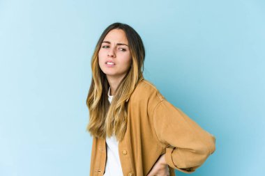 Mavi arka planda izole edilmiş beyaz bir kadın sırt ağrısı çekiyor..