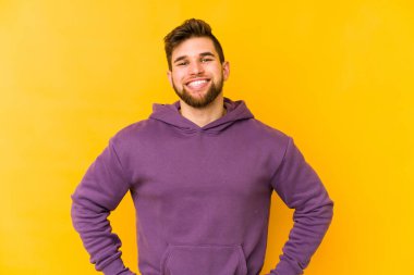 Sarı arka planda izole edilmiş genç beyaz adam ellerini kalçalarına koyuyor..