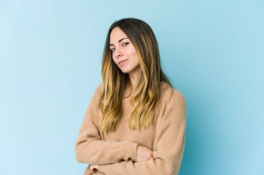 Kafkasyalı genç bir kadın mavi arka planda izole edilmiş şüpheli, belirsiz, seni muayene ediyor..