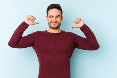 Mavi arka planda izole edilmiş genç beyaz adam gururlu ve kendinden emin hissediyor, örnek olarak.