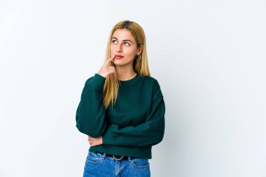 Beyaz arka planda izole edilmiş genç sarışın kadın şüpheli ve şüpheci bir ifadeyle yana bakıyor..