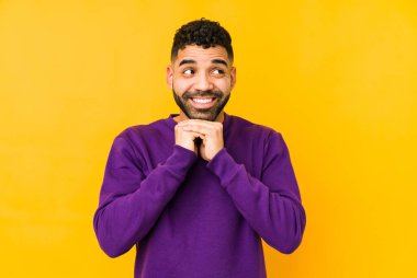 Genç, melez, yalıtılmış Arap bir adam ellerini çenesinin altında tutuyor ve mutlu bir şekilde yan tarafa bakıyor..