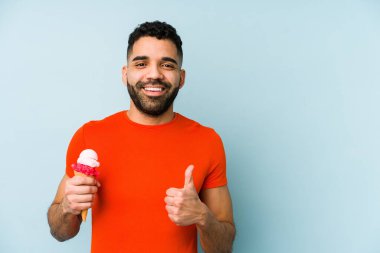 Dondurma tutan genç latin adam izole edilmiş gülümsüyor ve başparmağını kaldırıyor.