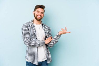 Mavi arka planda izole edilmiş genç beyaz adam işaret parmağıyla işaret ederek gülümsüyor..