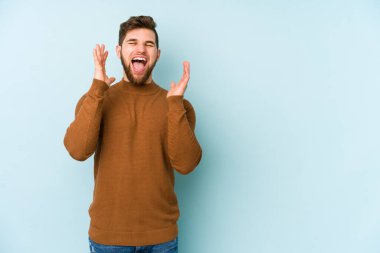 Mavi arka planda izole olmuş genç beyaz adam yüksek sesle gülüyor ve elini göğsüne koyuyor..
