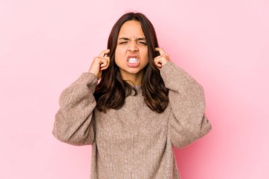 Latin kökenli genç bir kadın kulaklarını parmaklarıyla kapatıyor, gürültülü bir ortam yüzünden stresli ve çaresiz..