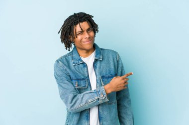 Kot ceket giyen genç siyah bir adam gülümsüyor ve boş alanda bir şeyler gösteriyor..