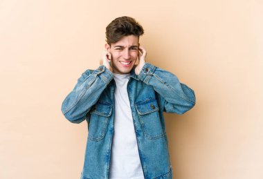 Beyazlı genç bir adam bej arka planda izole edilmiş kulakları elleriyle kapatıyor..