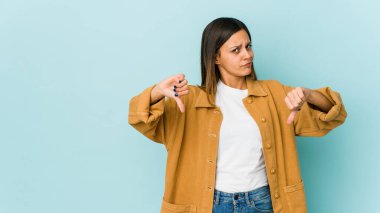 Mavi arka planda izole edilmiş genç bir kadın baş parmağını aşağı gösteriyor, hayal kırıklığı konsepti..