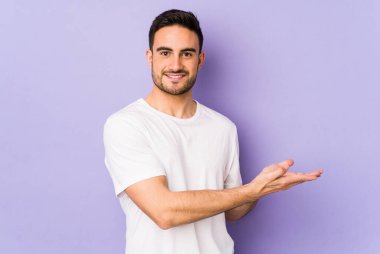 Mor arka planda izole edilmiş genç beyaz bir adam bir palmiyenin üzerinde bir kopya alanı tutuyor..