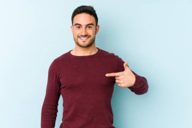 Mavi arka planda izole edilmiş genç beyaz adam bir gömlek fotokopi alanını işaret ediyor, gururlu ve kendinden emin.