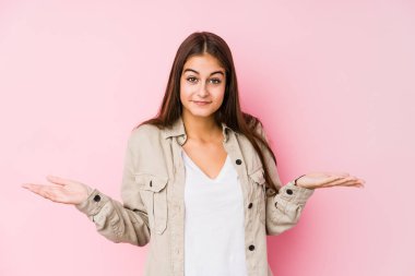 Pembe arka planda poz veren beyaz bir kadın sorgulama sırasında omuz silkiyor ve şüphe duyuyor..