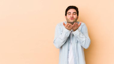Bej arka planda izole edilmiş genç bir adam dudakları katlıyor ve hava öpücüğü vermek için avuç içleri tutuyor..