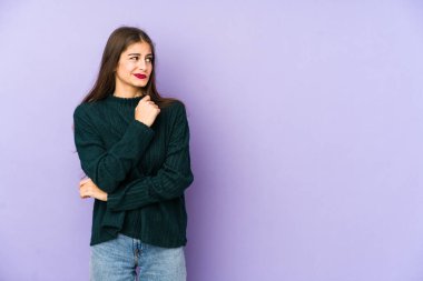 Mor arka planda soyutlanmış, kafası karışmış, şüpheli ve güvensiz genç bir beyaz kadın..