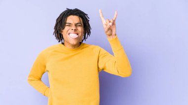 Rasta saç stili giyen genç siyah adam parmaklarıyla kaya hareketi yapıyor.