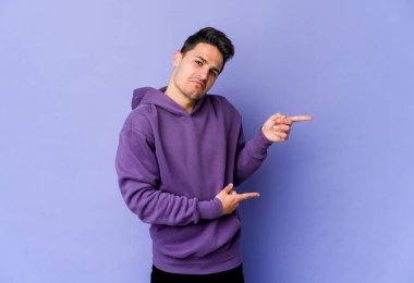 Mor arka planda izole edilmiş genç beyaz adam işaret parmağıyla fotokopi alanını işaret ederek şok oldu..