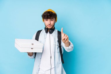 Elinde pizza tutan genç bir Arap öğrenci parmağıyla bir numarayı gösteriyor..