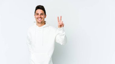 Beyaz arka planda izole edilmiş genç beyaz bir adam zafer işareti gösteriyor ve gülümsüyor..