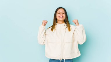 Mavi arka planda izole edilmiş genç bir kadın zaferi, tutkuyu ve coşkuyu, mutlu ifadeyi kutluyor..