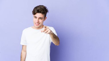 Mor arka planda izole edilmiş genç beyaz adam parmaklarıyla ön tarafı işaret ediyor..