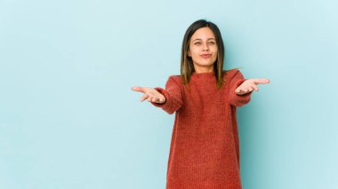 Mavi arka planda izole edilmiş genç bir kadın. Dudakları kıvrılmış ve avuç içleriyle hava öpücüğü yolluyor..