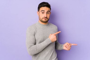 Mor arka planda izole edilmiş genç beyaz adam işaret parmağıyla fotokopi alanını işaret ederek şok oldu..