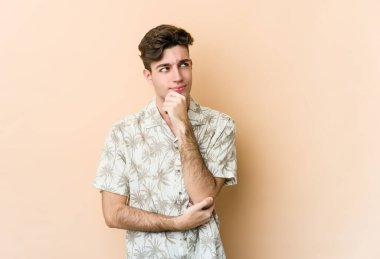 Beyaz tenli genç adam bej arka planda izole edilmiş. Rahatlamış bir şekilde fotokopi odasına bakan bir şey düşünüyor..