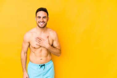 Sarı arka planda mayosu olan genç beyaz adam alabalıkları yüksek sesle göğsüne bastıran beyaz genç adam..