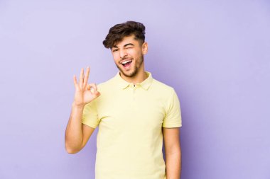 Mor bir arka planda izole edilmiş genç bir Arap göz açıp kapayıncaya kadar iyi bir el hareketi yapar..